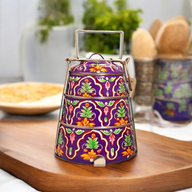 A hand-painted 3-tier steel tiffin box in purple with intricate floral designs, displayed on a wooden table.