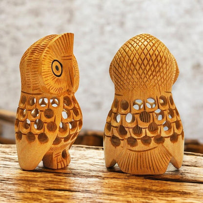 Two wooden owl carvings on a wooden surface with a blurred background