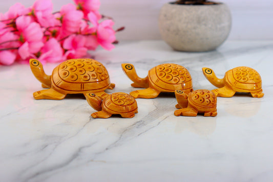 A set of five wooden tortoise figurines in various sizes, with intricate carvings, displayed on a marble surface with pink flowers in the background.