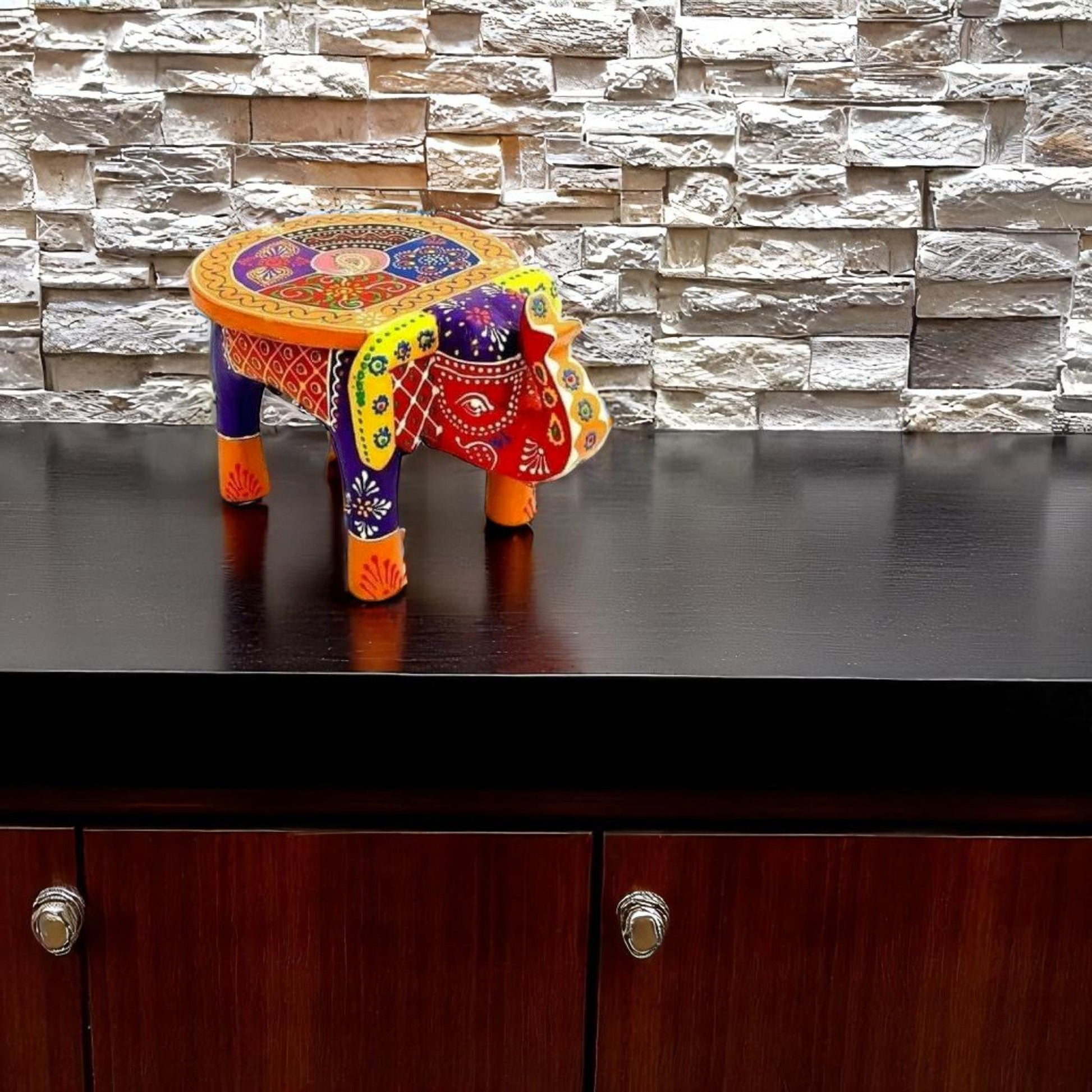 Colorful elephant-shaped table on a dark surface with a stone wall background