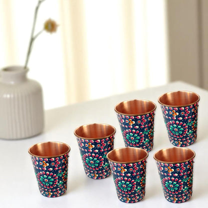 Set of six floral-patterned copper cups on a white surface with a blurred background