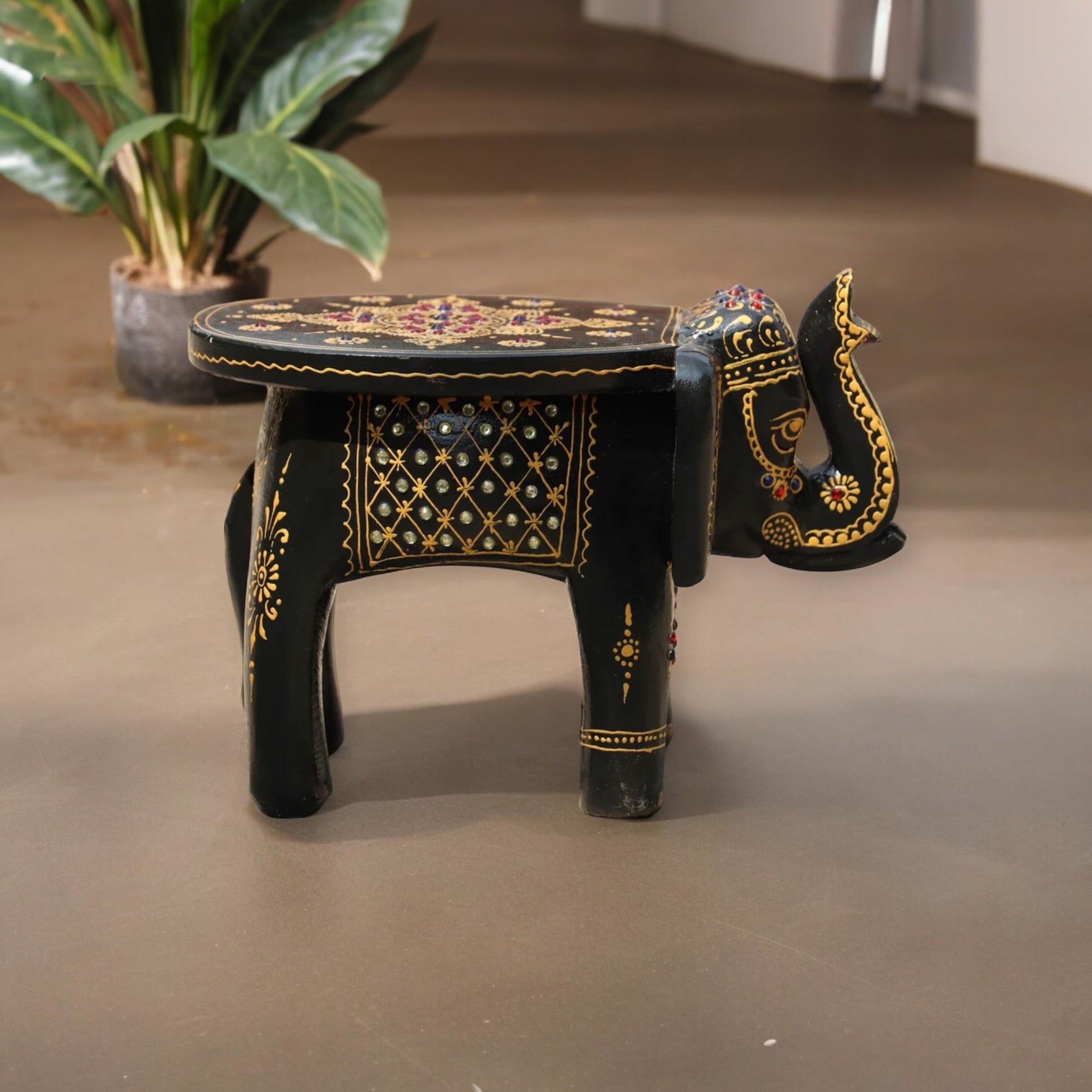 A hand-painted wooden elephant stool with intricate details and a colorful design, placed on a floor with a plant in the background.
