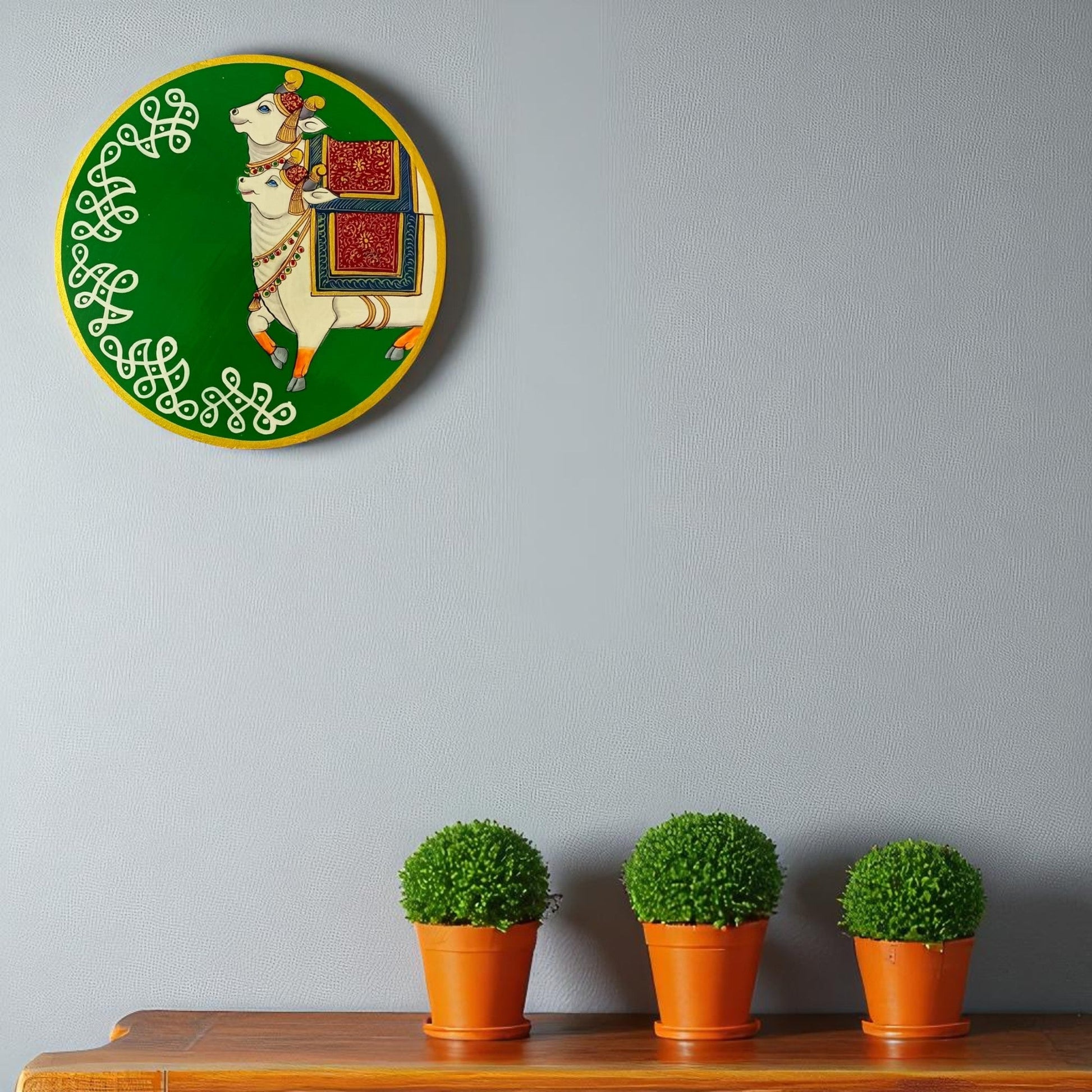 Decorative wall plate with a horse design on a green background, above three potted plants on a wooden surface.