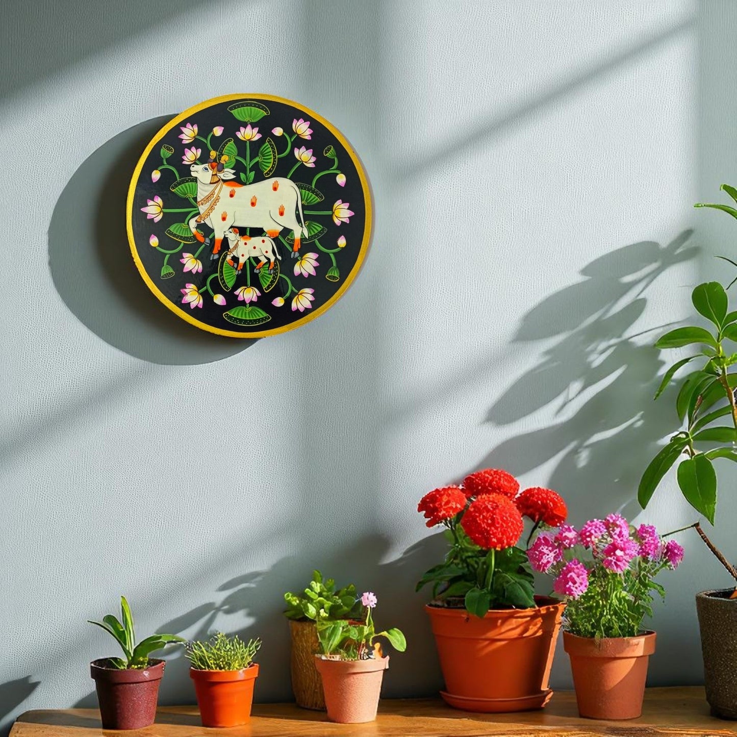 Decorative wall piece with cows and flowers on a light blue wall, below which are potted plants.