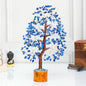 Decorative tree with blue stones on a white surface with a wooden box and small statue in the background.