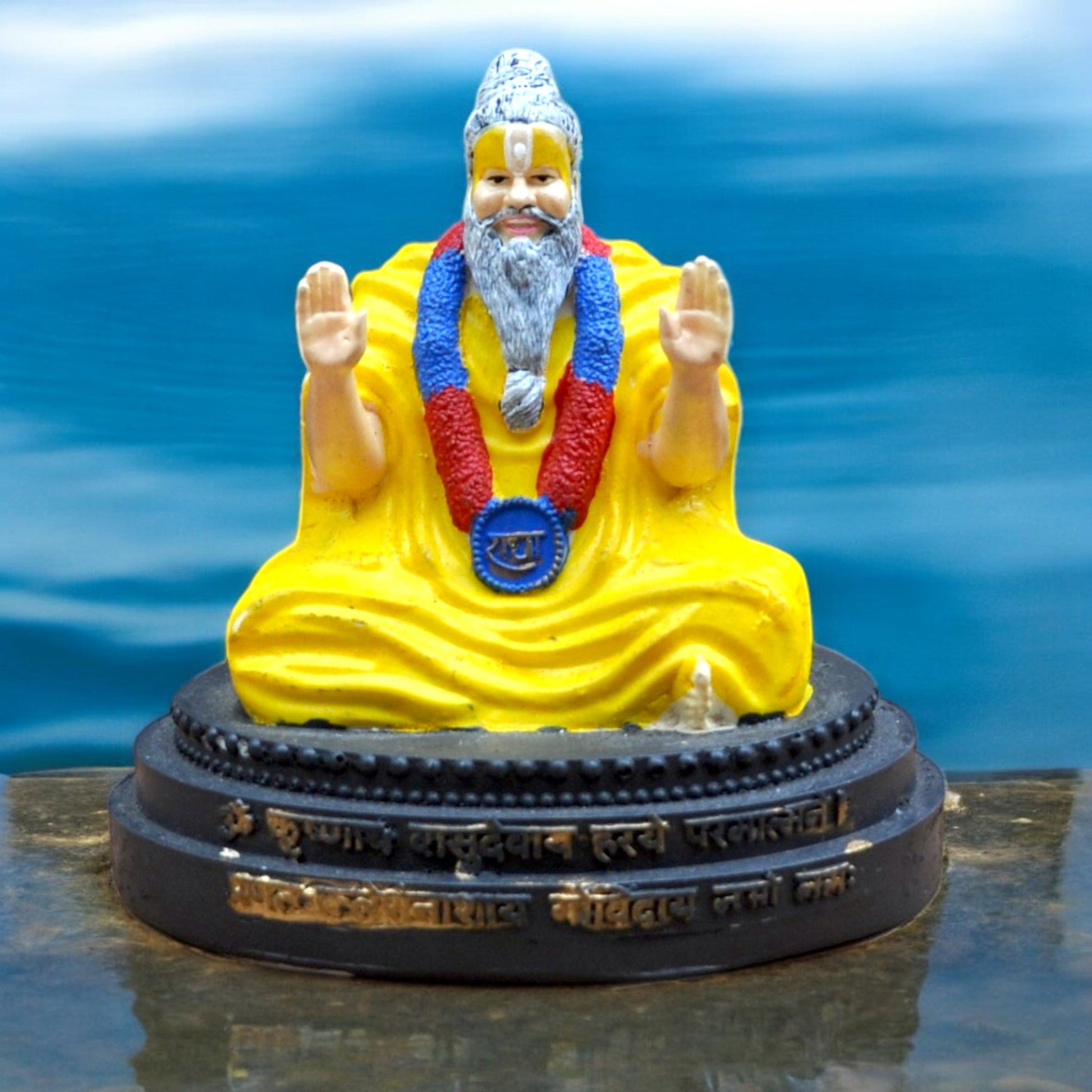 Statue of a religious figure in yellow robes with a blue and red headdress on a reflective surface.
