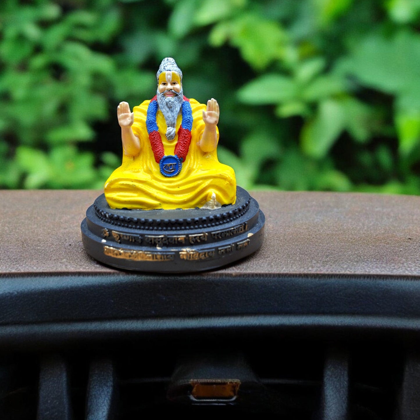 Statue of a seated figure in yellow robes on a black base with a green blurred background