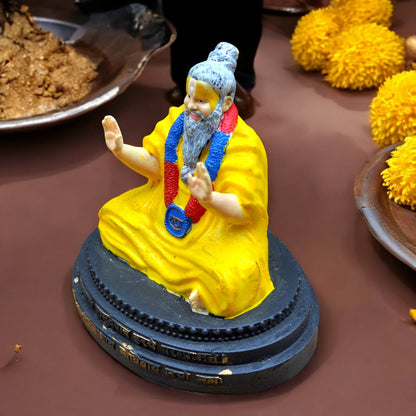 Statue of a figure in yellow robes with colorful accessories on a dark base, surrounded by yellow spherical objects.