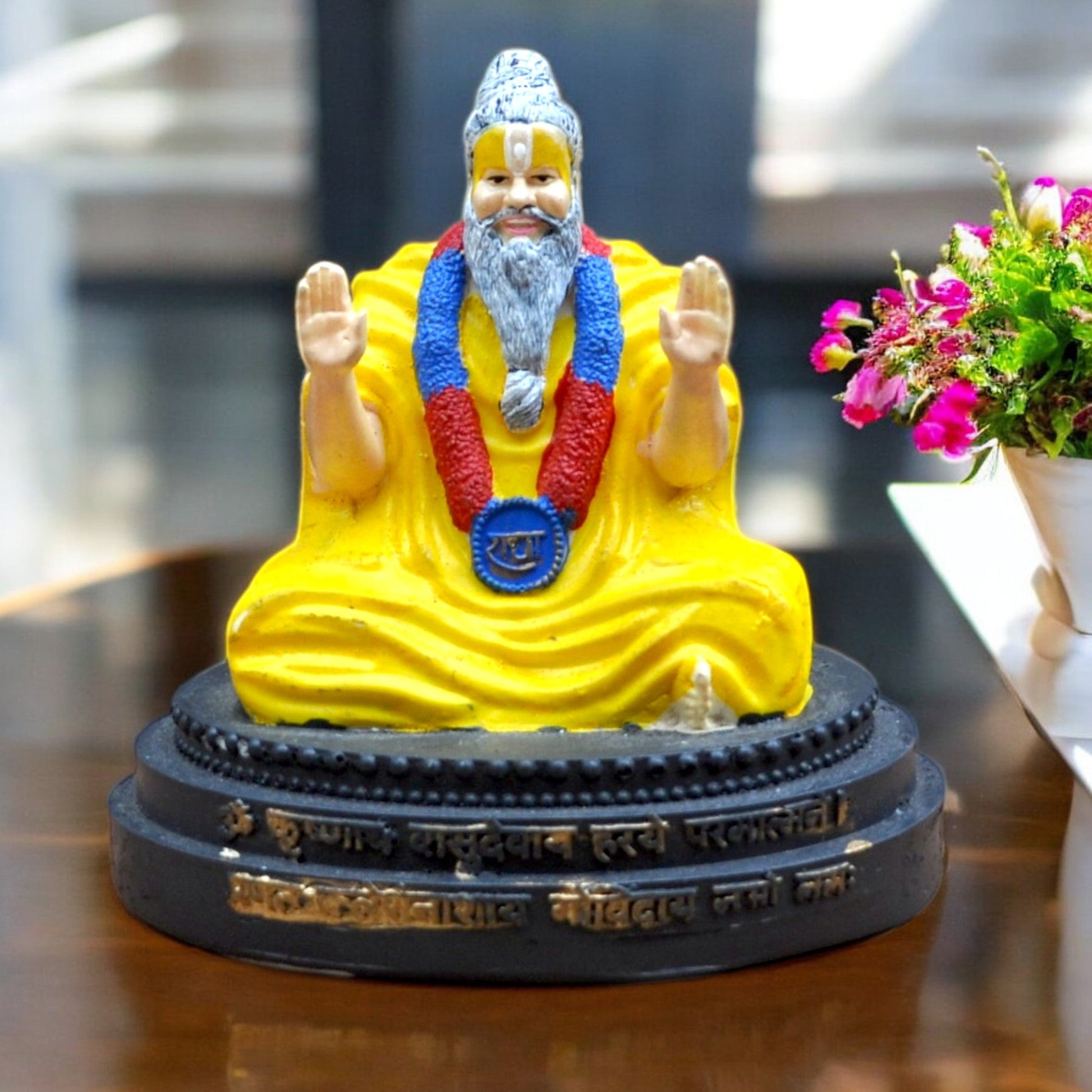 Statue of a religious figure in yellow robes with a blue and red headdress on a dark base.