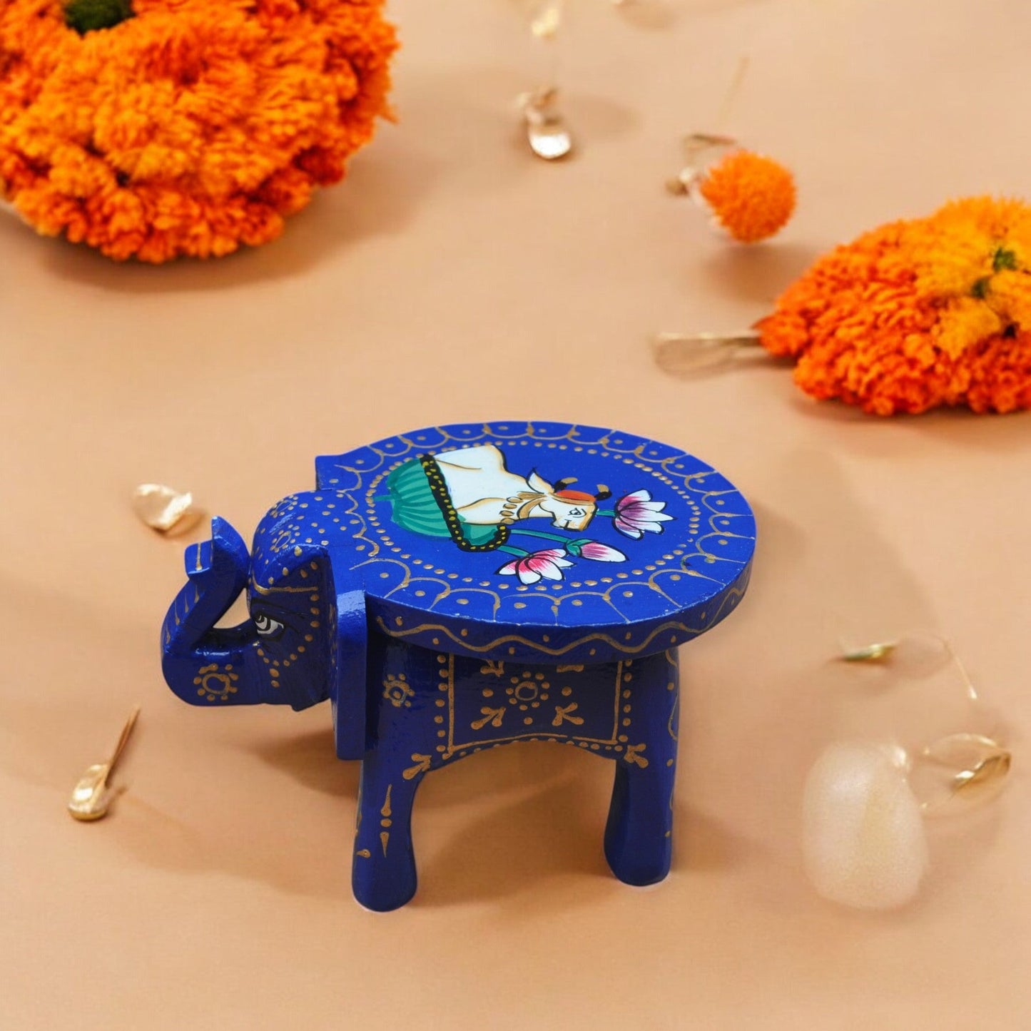 Blue elephant-shaped stool with a colorful design on a beige background with orange flowers.