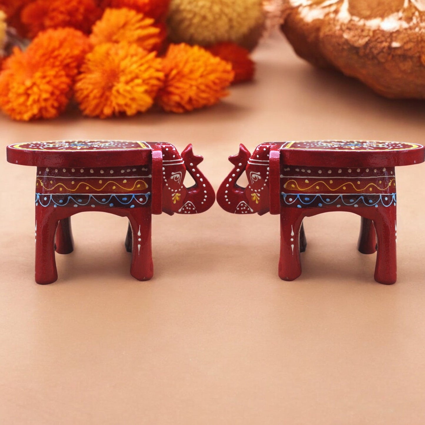 Two red elephant-shaped stools with intricate designs on a beige background.