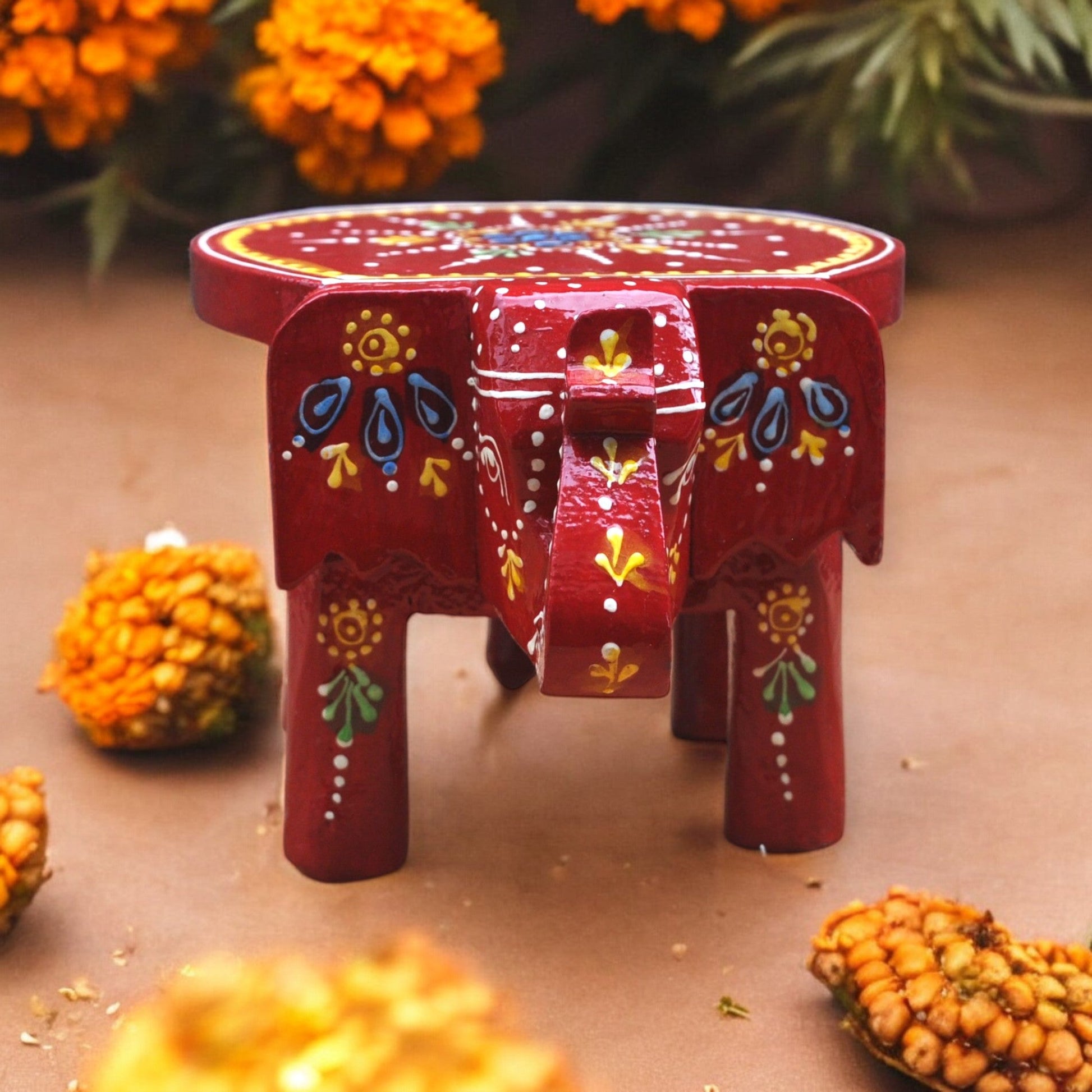 Decorative red elephant with floral patterns on a brown surface with orange flowers in the background