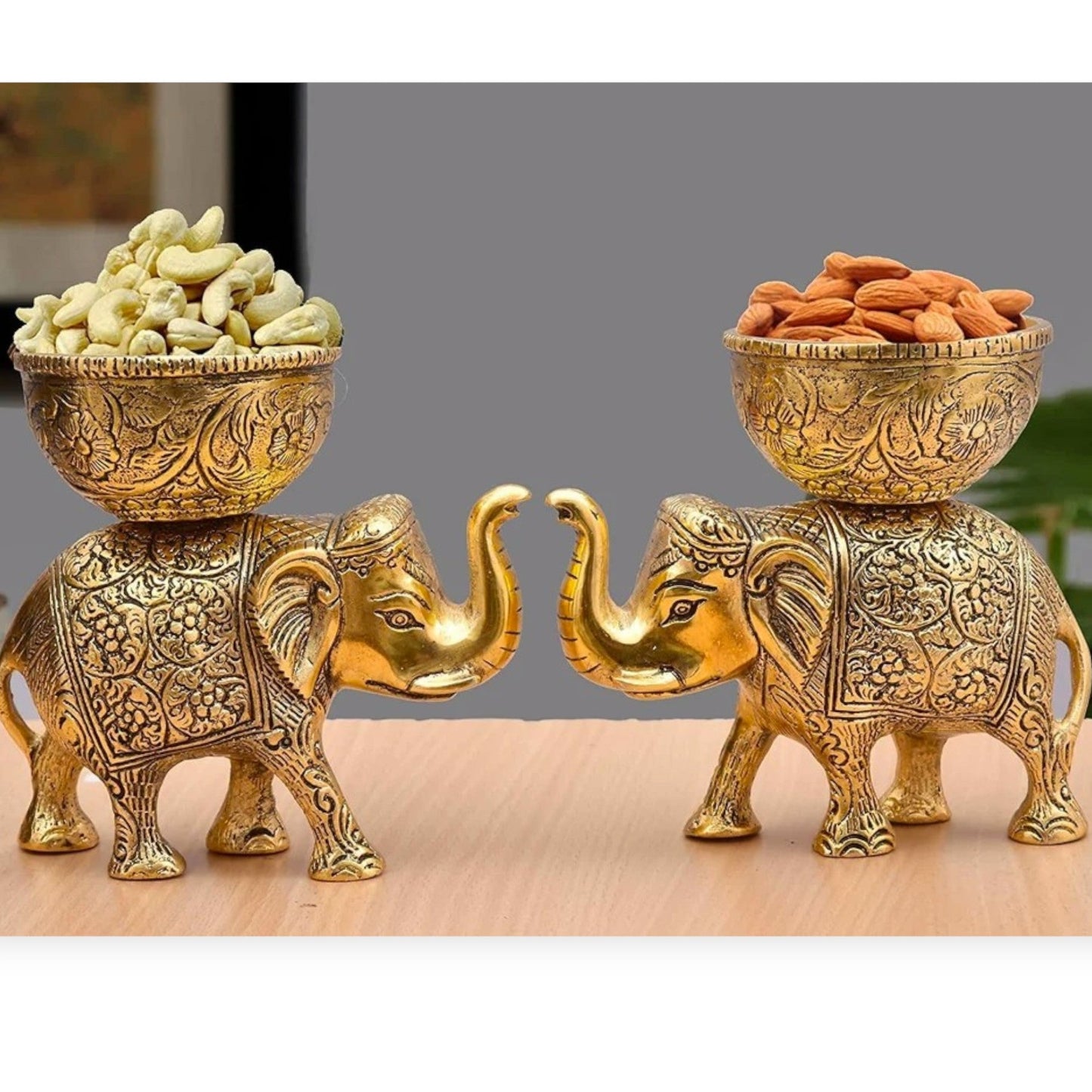 Two ornate gold elephant statues with bowls of snacks on a wooden surface.