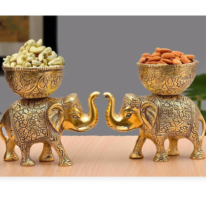 Two ornate gold elephant statues with bowls of snacks on a wooden surface.