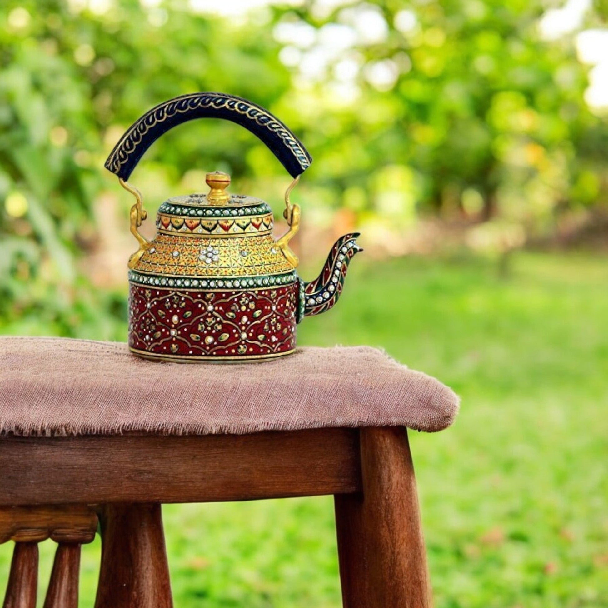 A colorful hand-painted aluminum tea kettle figurine with a wooden handle, displayed on a wooden surface.