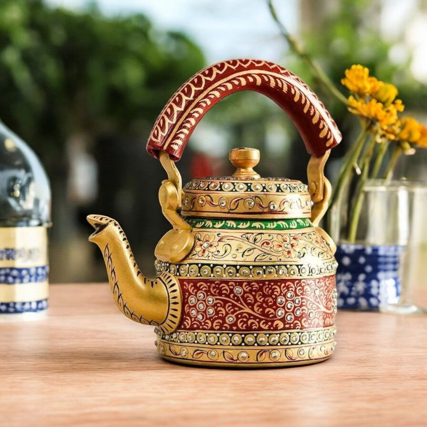 A colorful hand-painted aluminum tea kettle figurine with a wooden handle, displayed on a table.