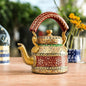 A colorful hand-painted aluminum tea kettle figurine with a wooden handle, displayed on a table.