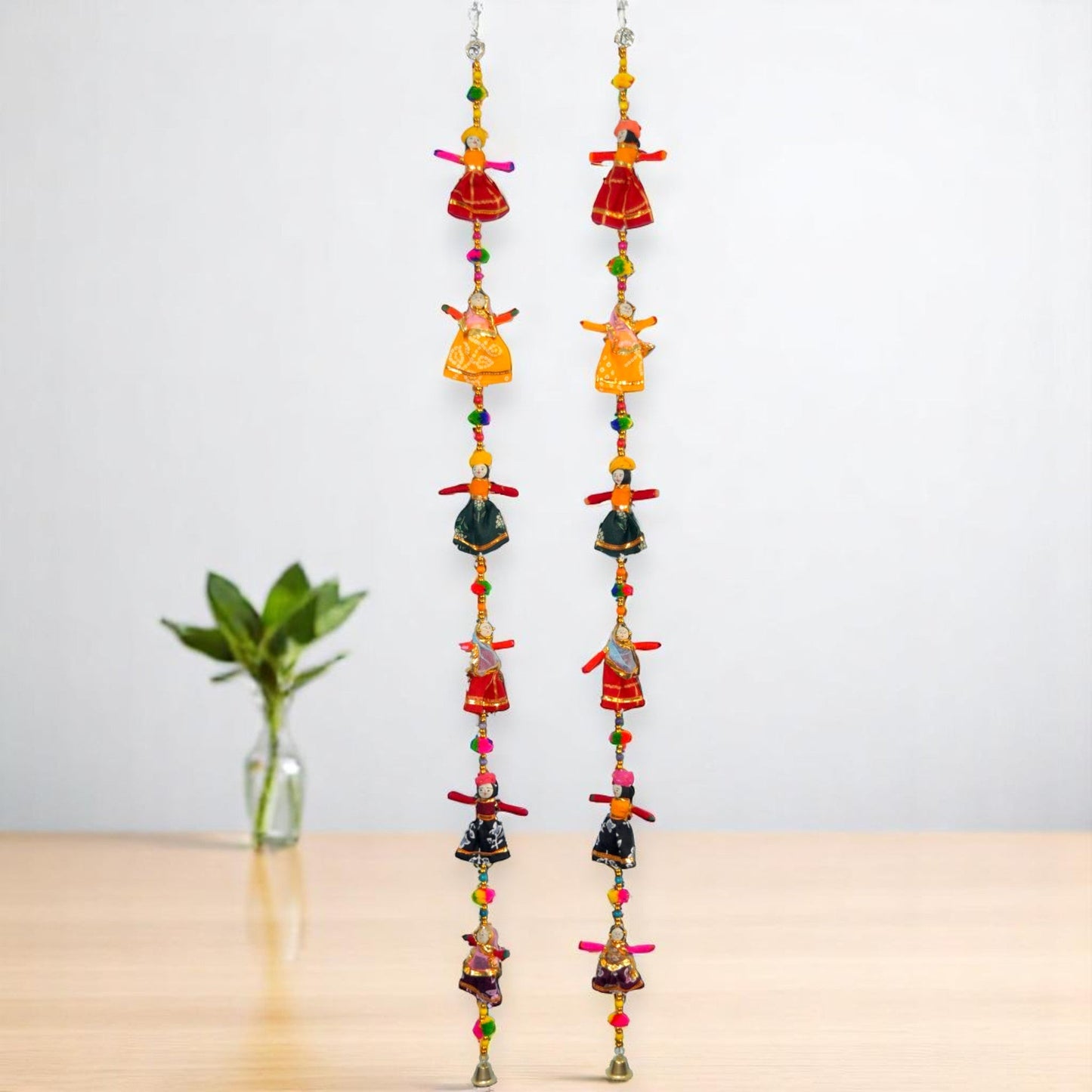 Two sets of wooden puppet hangings with colorful accents, displayed against a neutral background with a plant to the side.